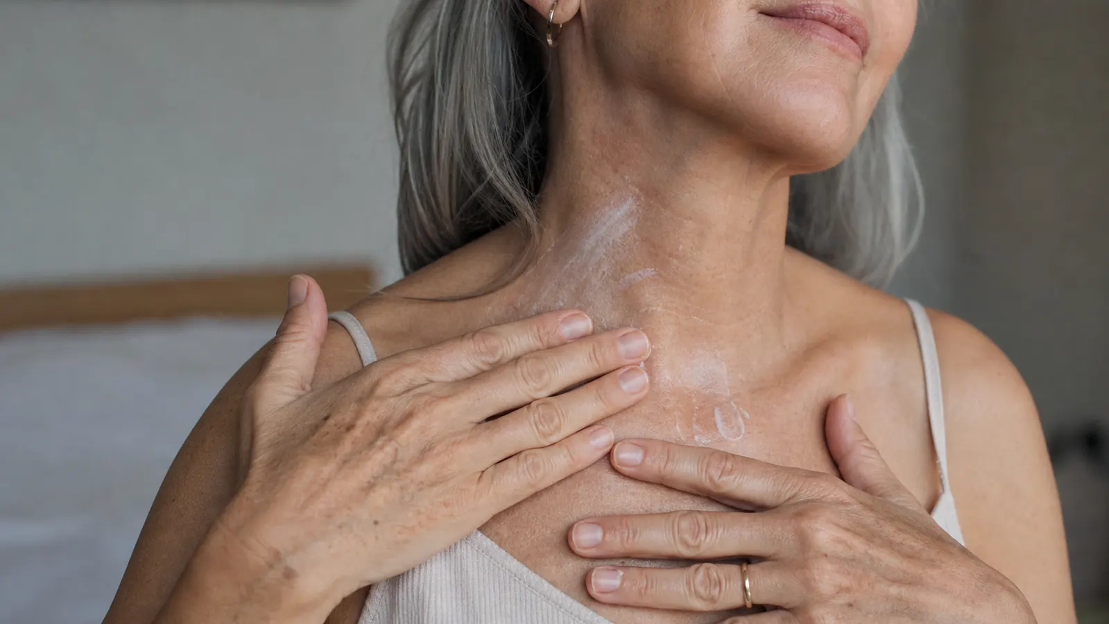 Close-up of a woman's hands smoothing cream along her collarbone and neck